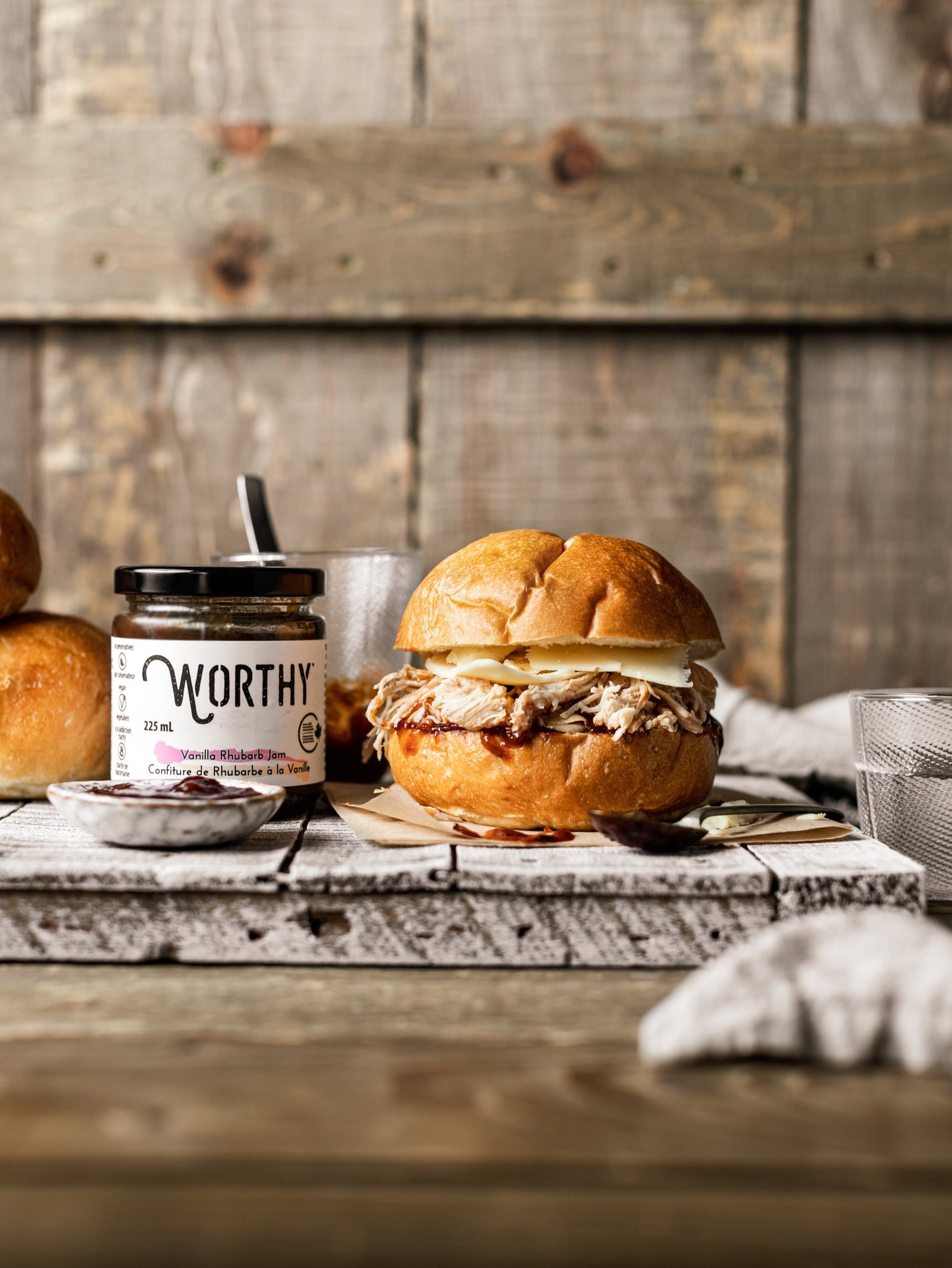 Kaiser bun filled with pulled chicken and cheese topped with Rhubarb ketchup made from Worthy’s Vanilla Rhubarb jam in a rustic setting.