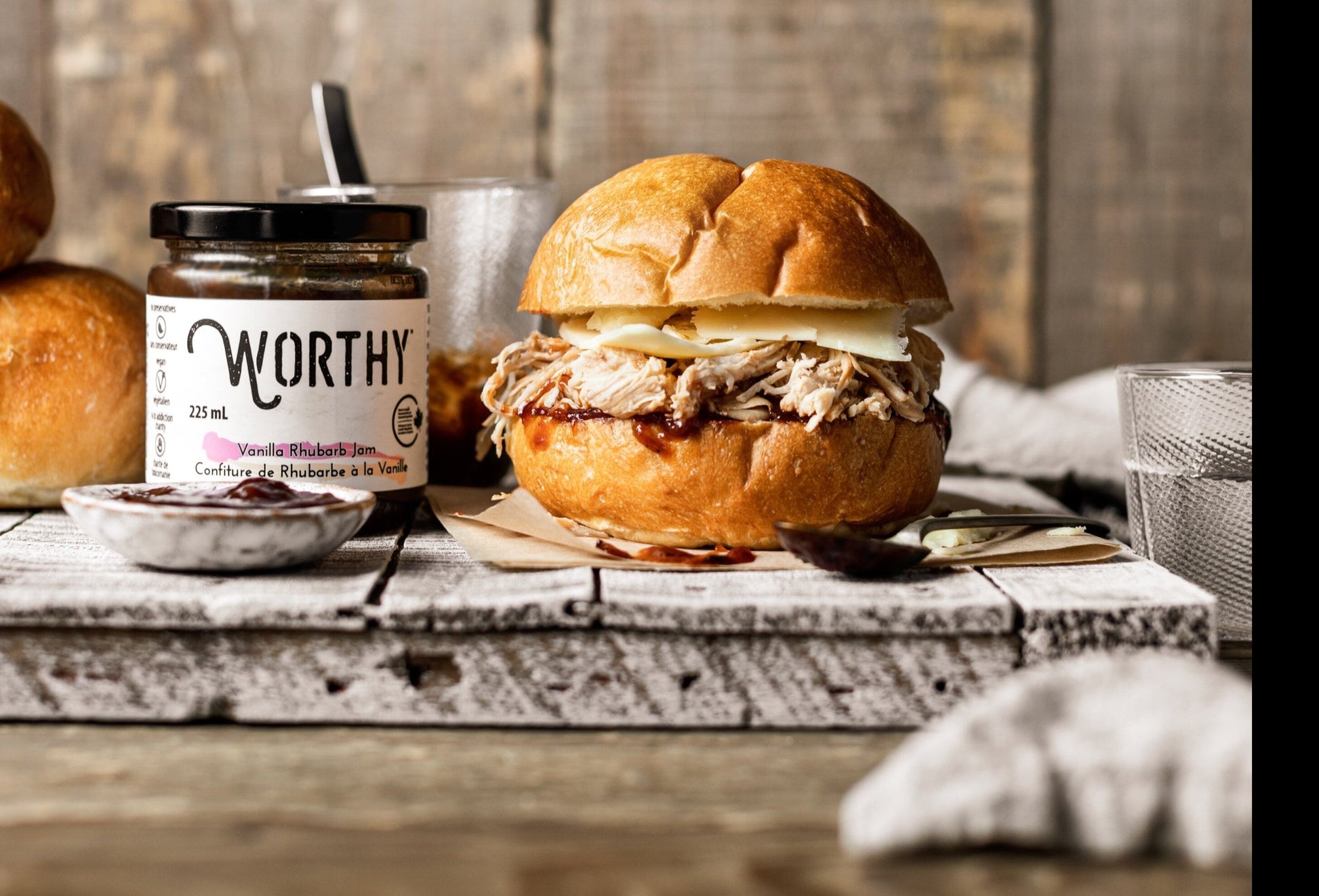 Kaiser bun filled with pulled chicken and cheese topped with Rhubarb ketchup made from Worthy’s Vanilla Rhubarb jam in a rustic setting.