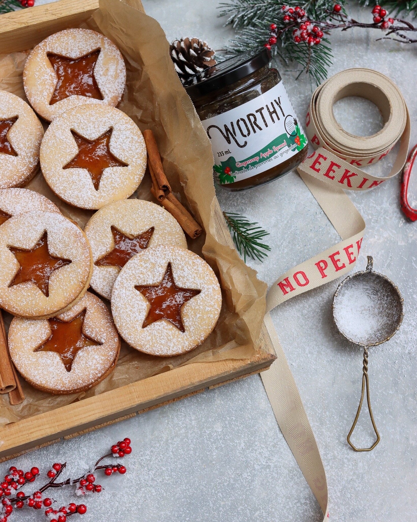 Linzer cookies with a star shaped window revealing filling, made with Worthy's Gingersnap Apple Spread, dusted with powdered sugar in a Christmas setting.