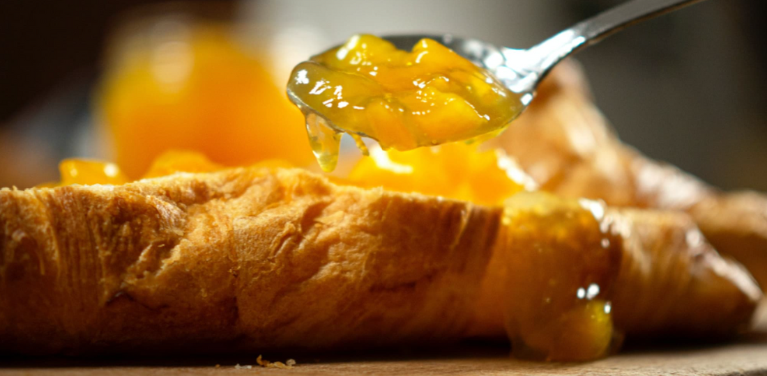 a heaping spoonful of peach jam hovering over a croissant.