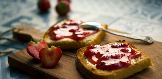 toast with strawberry jam spread over the toast and a strawbery cut in half beside the toast.
