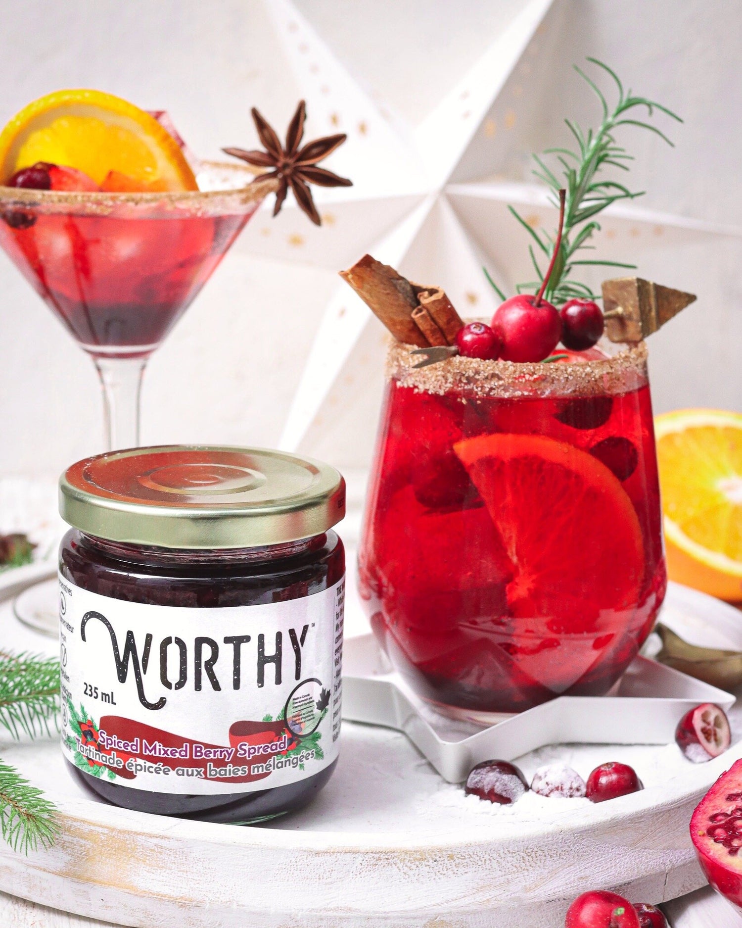 Pomegranate and berry mocktail with a cinnamon sugar rim topped with fruit and spices made with Worthy’s Spiced Mixed Berry spread in a Christmas setting.