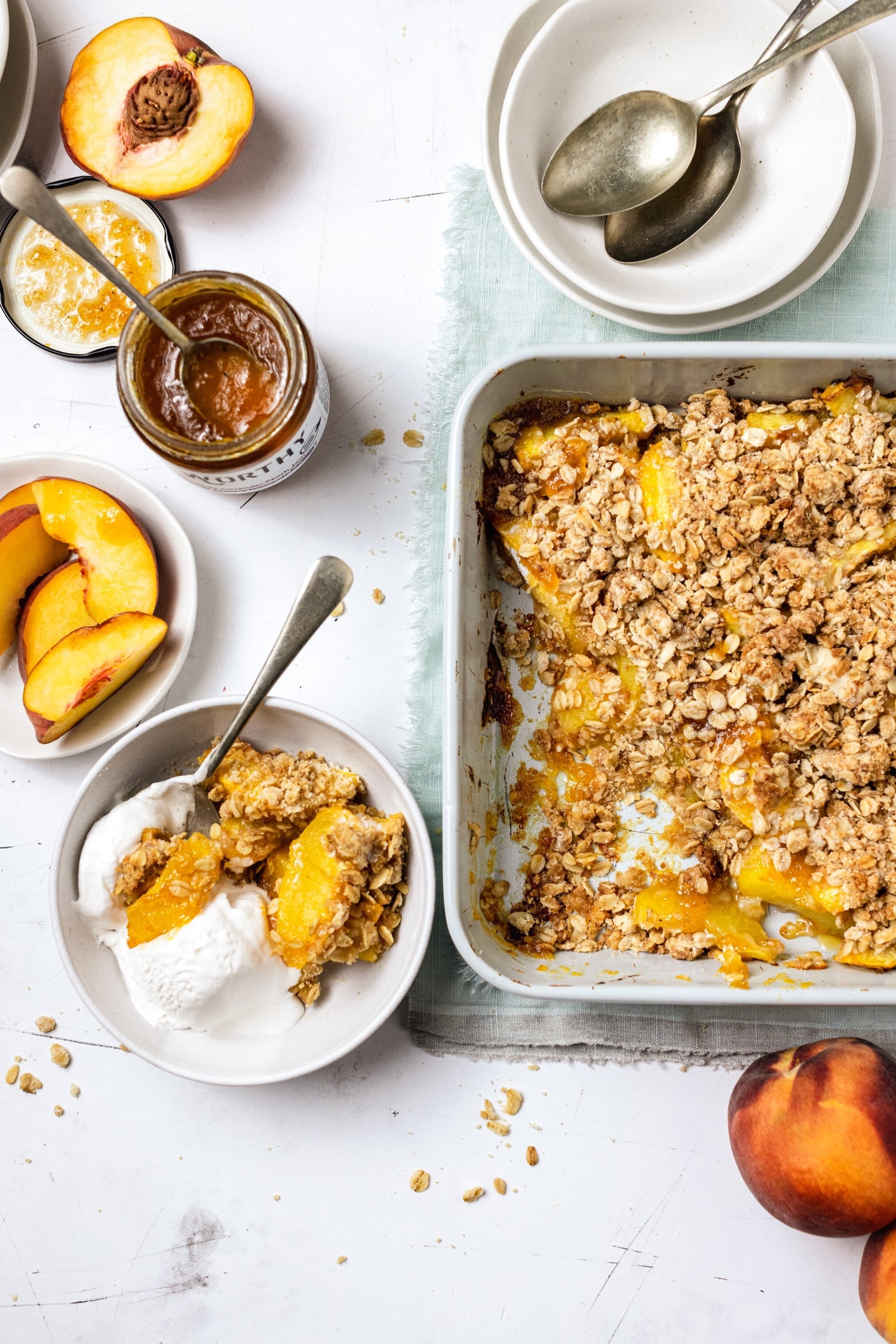A tray of baked peach crisp with Worthy’s Earl Grey Lavender jam filling next to a portion of the crisp in a bowl with vanilla ice cream.