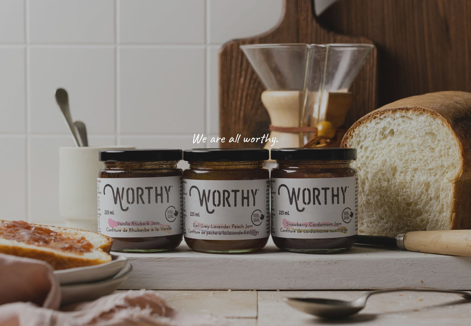 Three jars of Worthy jam on a cutting board in a kitchen setting with a quote that says "we are all worthy"