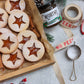 Linzer cookies with a star shaped window revealing filling, made with Worthy's Gingersnap Apple Spread, dusted with powdered sugar in a Christmas setting. 