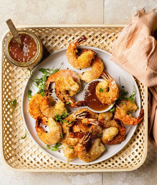 Plate of coconut-crusted shrimp with one shrimp dunked in a spicy dipping sauce made with Worthy’s Earl Grey Lavender Peach jam and red pepper flakes.