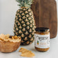 Worthy's Hot Pineapple Turmeric Salsa beside a wooden bowl of tortilla chips and a pineapple and cutting board in the background.