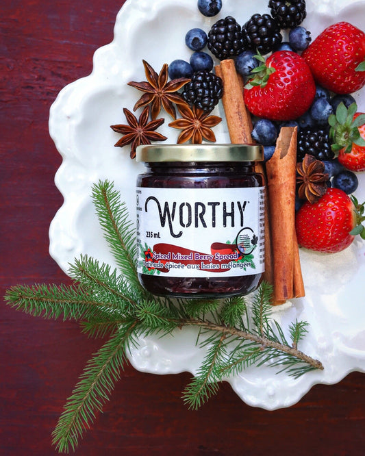 Worthy's Spiced Mixed Berry Spread displayed on a white plate alongside an assortment of strawberries, blackberries and blueberries with cinnamon sticks, star anise, and a decorative pine branch.