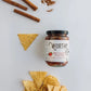 Worthy's Warm Cinnamon Tomato Salsa displayed on a simple white background alongside a pile of tortilla chips and cinnamon sticks.