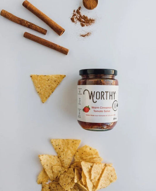 Worthy's Warm Cinnamon Tomato Salsa displayed on a simple white background alongside a pile of tortilla chips and cinnamon sticks.
